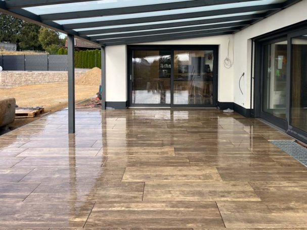 Terrasse mit Fliesen, überdacht, moderne Architektur, Blick auf einen Garten.