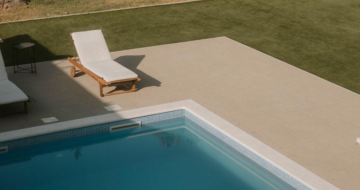 Pool mit Liegen und gepflastertem Bereich auf grüner Rasenfläche.