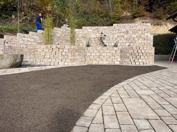Pflasterweg vor einer Mauer aus gestapelten Steinen mit Pflanzen.