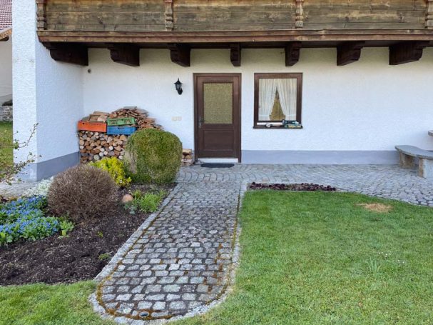 Eingang zu einem Haus mit Pflastersteinen, Garten und einer Sitzecke.