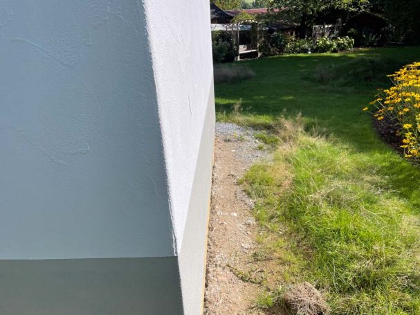 Graue Wand mit scharfem Winkel, Gras und Blumen im Garten im Hintergrund.