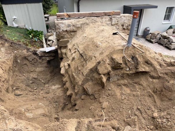 Baggeraushebung mit Sand, teilweise aufgeschütteter Boden, angrenzendes Gebäude sichtbar.