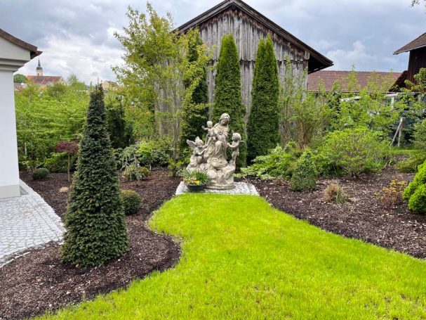 Skulptur im Garten, umgeben von gepflegtem Rasen und Bäumen.