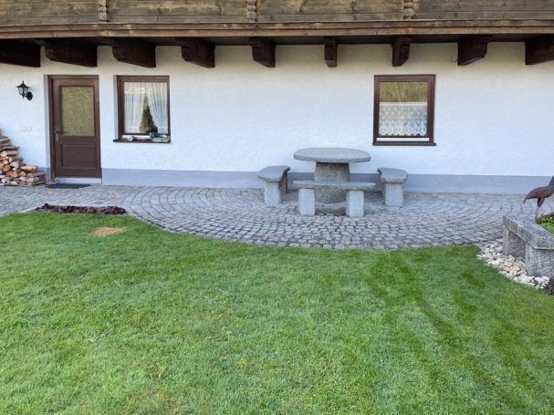 Ein gepflasterter Außenbereich mit einem Tisch und Bänken vor einem Haus.