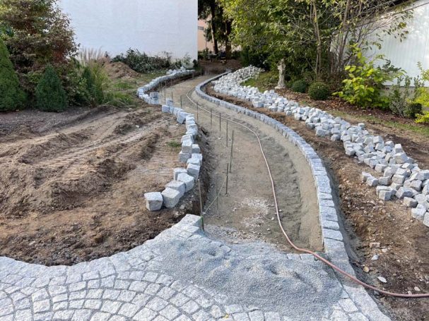Gepflasterter Weg in einer Gartenlandschaft, umgeben von Erde und kleinen Steinen.