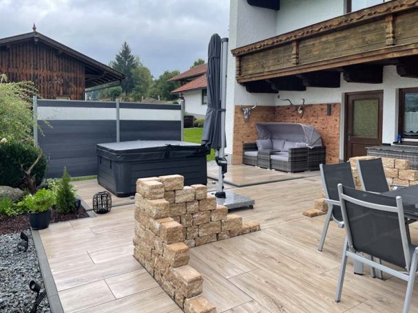 Terrasse mit Holzofen, Gartenmöbeln und Whirlpool, umgeben von Bäumen und Häusern.