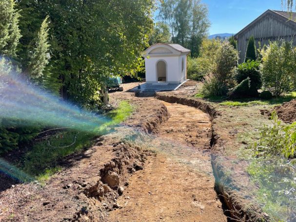 Weg mit Erdboden, umgeben von Bäumen, führt zu einer kleinen weißen Kapelle.