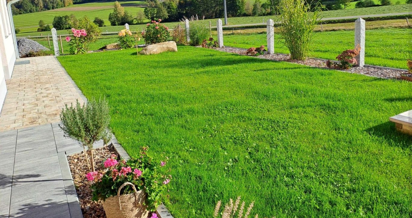 Grüner, gepflegter Garten mit Blumenbeeten und weißem Zaun.