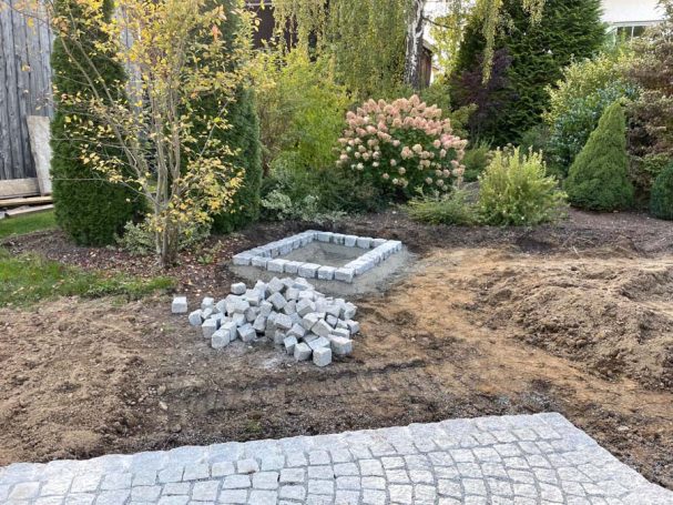 Gartenbereich mit einer verspäteten Bepflanzung und einer gepflasterten Fläche.