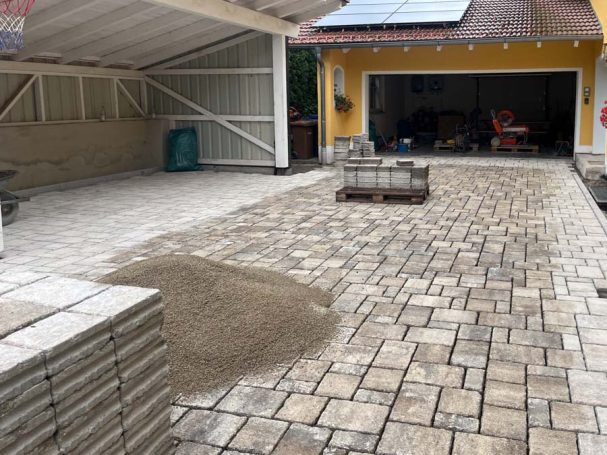 Gepflasterte Fläche mit einigen Sandhaufen und gestapelten Pflastersteinen.