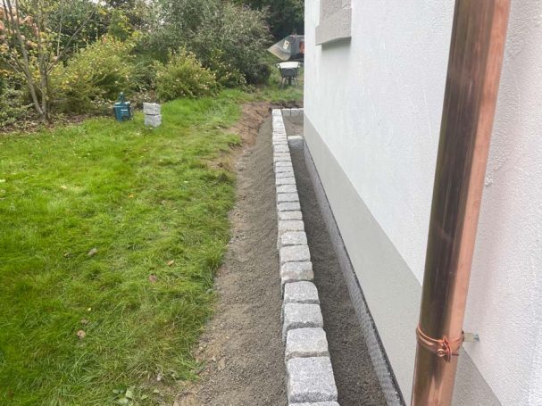 Mauersteine entlang einer Gartenkante neben einem weißen Gebäude.