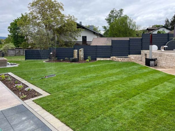 Pflegeleichter Garten mit Rasen, modernem Zaun und Bepflanzung.