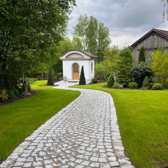 Ein geschwungener Steinweg führt zu einem kleinen, charmanten Gebäude in einem Garten.