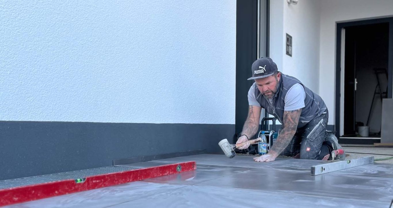 Handwerker bearbeitet den Fußboden mit einer Kelle und Werkzeug.