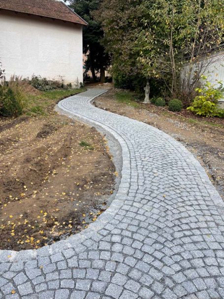 Ein gewundener Pflasterweg führt zwischen Bäumen zu einem Haus.