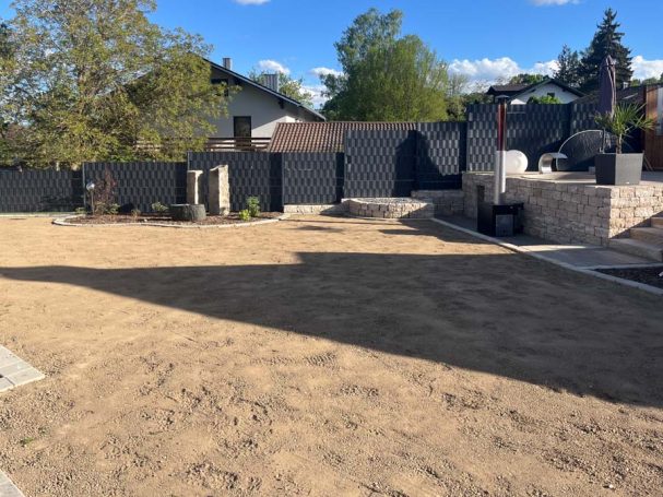 Neuer, unbepflanzter Gartenbereich mit sandigem Boden und schattenspendenden Bäumen.