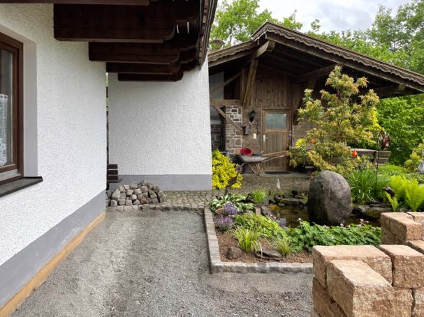 Einfamilienhaus mit Garten, Teich und Steinpflaster im Vordergrund.