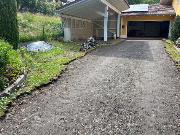 Schotterauffahrt neben einem Haus mit Gartenbereich und Überdachung.