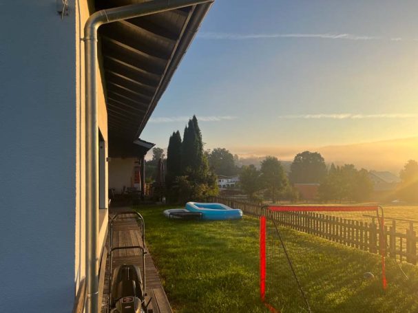 Morgensonne über einer Wiese mit einem blauen Pool und Zäunen im Hintergrund.