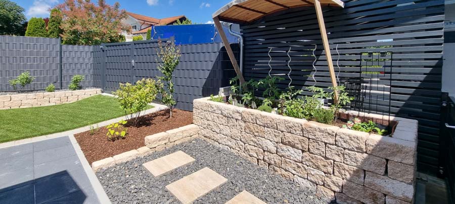 Gepflegter Garten mit Steinen, Pflanzen und einer überdachten Sitzecke.