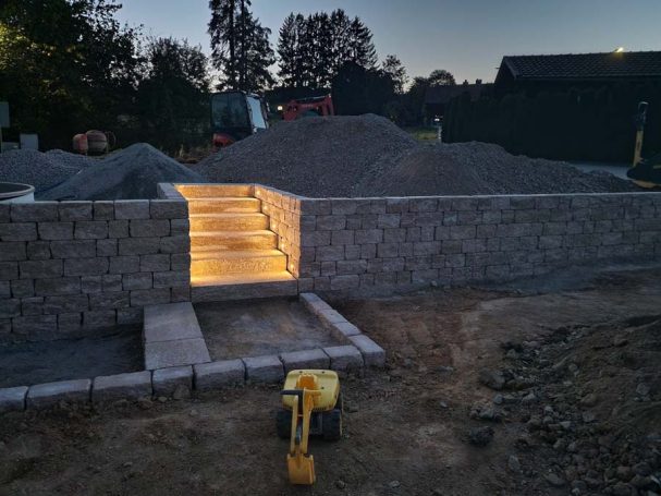 Beleuchtete Steinstufen führen in einen Grabensockel, umgeben von Erdhügeln.