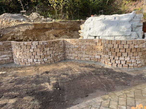 Ein Baustellenbereich mit einer Mauer aus Steinen und einem Erdhügel im Hintergrund.