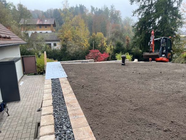 Bodenarbeiten in einem Garten mit unbefestigtem Bereich und Steinkante.