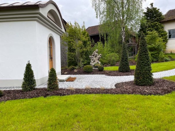 Gepflasterter Gartenweg mit Skulptur und grünen Hecken umgeben von Rasen.
