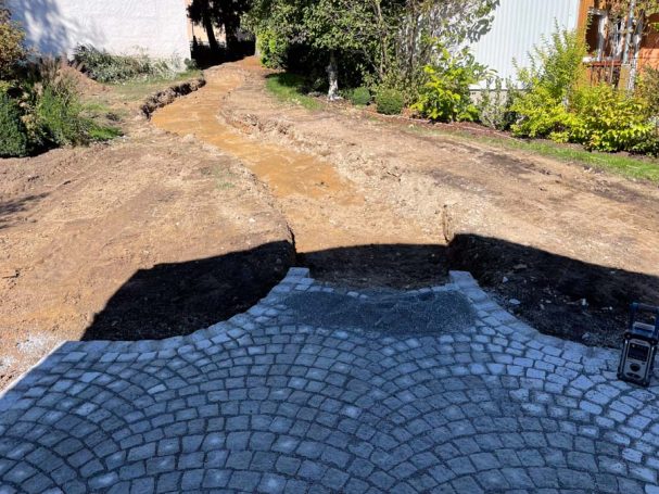 Ein unebener Weg mit Steinen und Erde, der zu einem Garten führt.