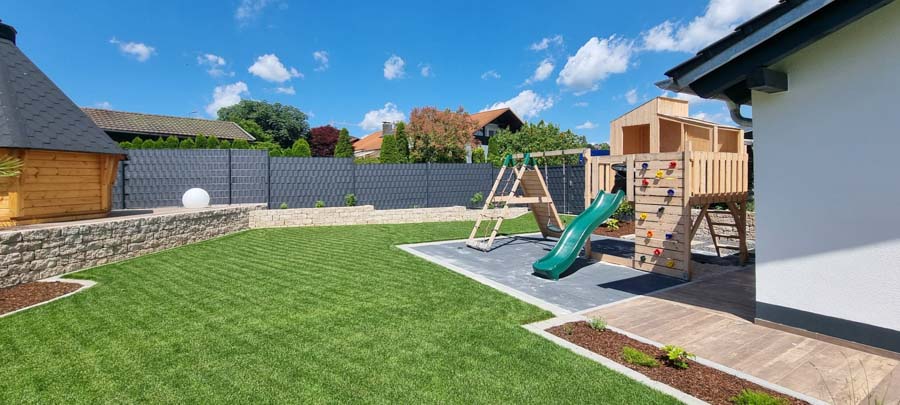 Spielplatz mit Rutsche und Schaukel in einem grünen Garten unter blauem Himmel.