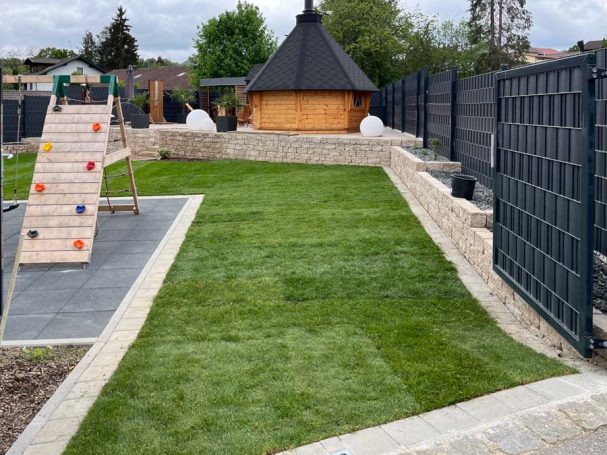 Garten mit Rasenfläche, Spielplatz und Holzhaus im Hintergrund.