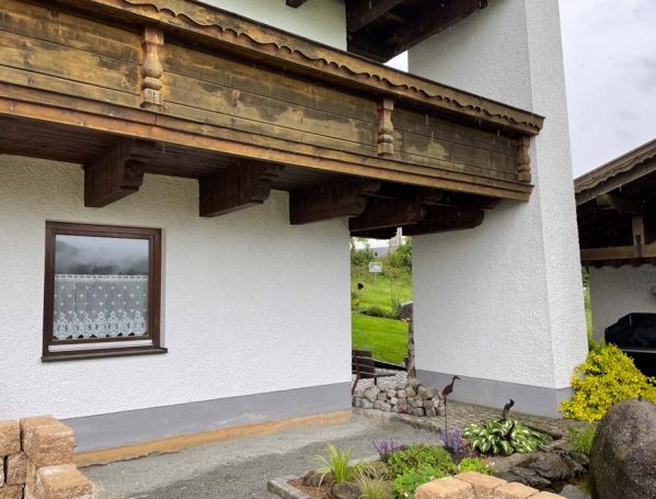 Bauernhaus mit Holzüberhang, Fenster und Gartenbereich im Vordergrund.