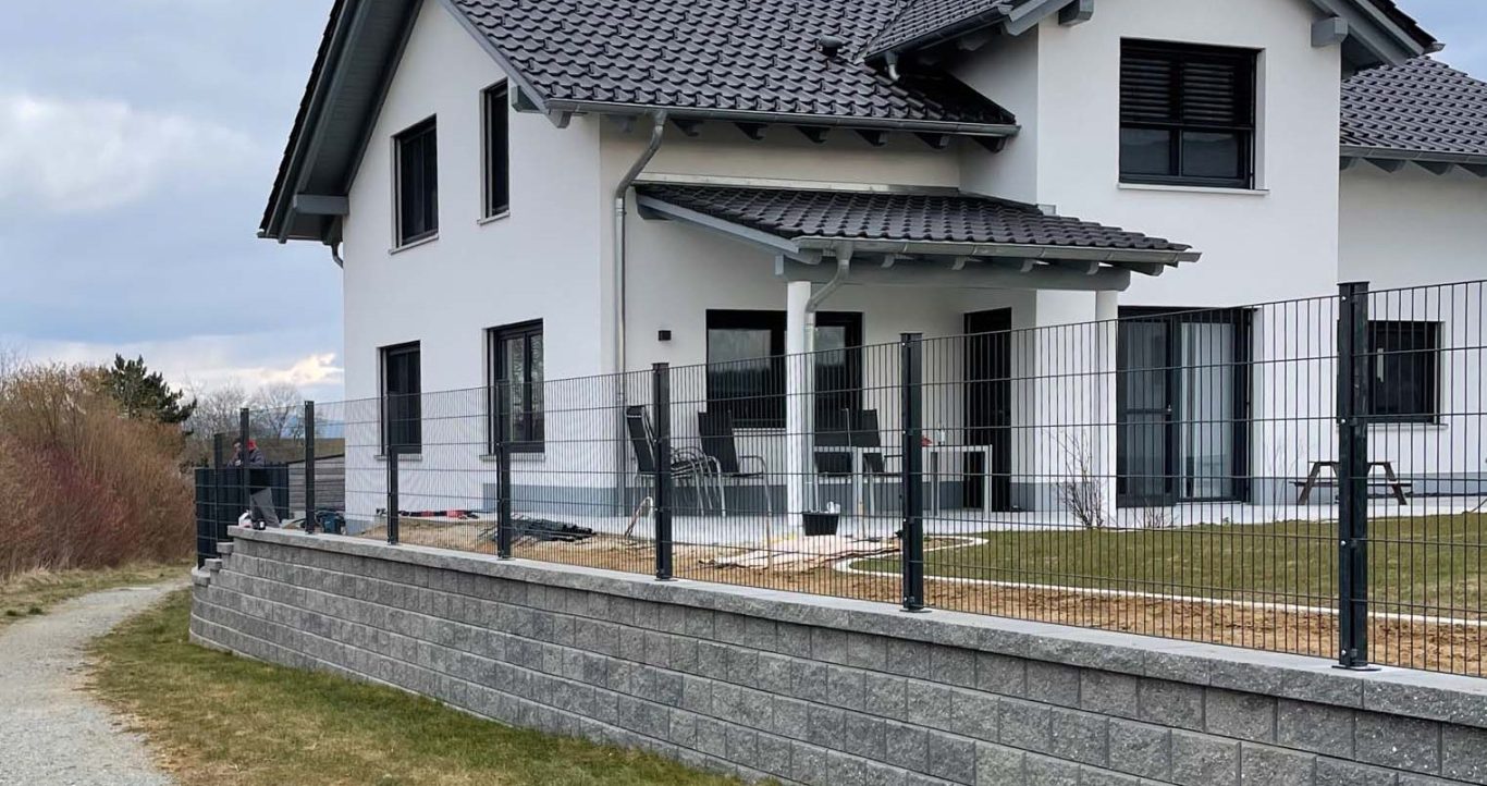 Modernes weißes Haus mit schwarzem Dach, umgeben von einem Zaun und einem Weg.