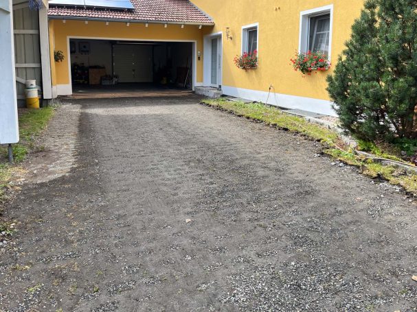 Schotterauffahrt vor einem gelben Haus mit Blumen und einer Garage.