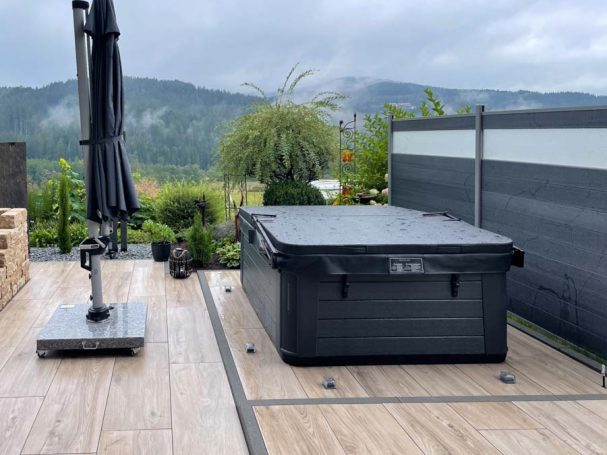 Ein Hot Tub auf einer Holzterrasse mit Sonnenschirm und grüner Landschaft im Hintergrund.