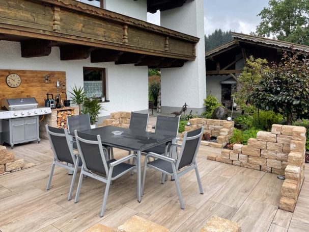 Gemütlicher Essbereich im Freien mit Tisch und Stühlen, umgeben von Pflanzen.